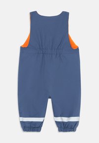 Blaue Latzhose mit orangefarbenen Akzenten, elastischem Bund und reflektierenden weißen Streifen an den Knöcheln. Hergestellt aus glattem, strapazierfähigem Stoff.
