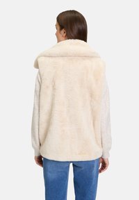 Faux-Fur-Weste in Creme mit breitem Kragen, strukturierter Oberfläche und lockerer Passform. Kombiniert mit hellblauen Jeans, strahlt sie ein weiches, gemütliches Aussehen aus.