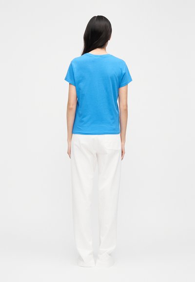 Mėlynas trumpomis rankovėmis marškinėlis iš minkštos medžiagos, derinamas su baltais platėjančiais kelnėmis, pasižymintis laisvu stiliumi ir paprastu, švariu dizainu.