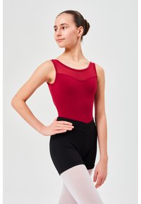 Roter, figurbetonter Tank-Leotard mit Mesh-Ausschnitt, kombiniert mit schwarzen hochgeschnittenen Shorts und hellrosa Strumpfhosen, auf einem neutralen Hintergrund.