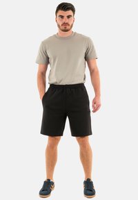 Una maglietta grigia in cotone con maniche corte abbinata a pantaloni corti neri. I pantaloni corti hanno una cintura elastica e tasche. Sneakers casual completano il look.