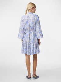 Robe fleurie bleu clair avec un ourlet en cascade, des manches trois-quarts et une taille cintrée. Elle présente des détails délicats en blanc et un tissu fluide.
