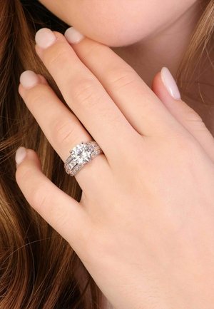 Diamond engagement ring with a large central stone, silver band, and smaller accent stones along the sides. Smooth, polished finish.