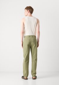 Lightweight olive green pants with a relaxed fit, featuring back pockets and a smooth fabric texture, paired with a white ribbed tank top.