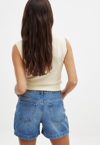 Gaiši brūns ribots topiņš ar īsām piedurknēm, kombinēts ar ziliem džinsu šortiem, kuriem ir klasiskas formas un kontrastējoša šuvšana uz kabatām.