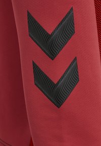 Rød atletisk stof har en tekstureret overflade med et sort chevron-design. Mønstret har bølgede linjer, som tilfører visuel interesse til materialet.