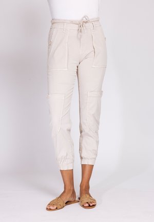 Light beige cropped cargo pants with large front pockets, elasticized ankles, and a drawstring waist, worn with tan slide sandals.
