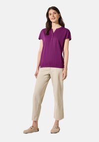 Top viola a maniche corte con scollatura henley e dettagli con bottoni, abbinato a pantaloni cropped beige chiaro e scarpe beige slip-on.