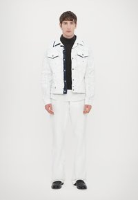 White denim jacket with blue accents, white turtleneck, and white flared pants. Black shoes complete the outfit. Minimalist design.