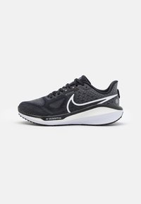 Chaussure de sport noire avec un dessus texturé, un swoosh Nike blanc, une semelle rembourrée et un motif de semelle en caoutchouc distinct.