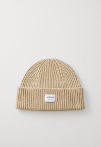 Bonnet beige en tricot avec une texture côtelée et un revers replié. Présente une petite étiquette blanche avec "ARKK" et "Copenhague."