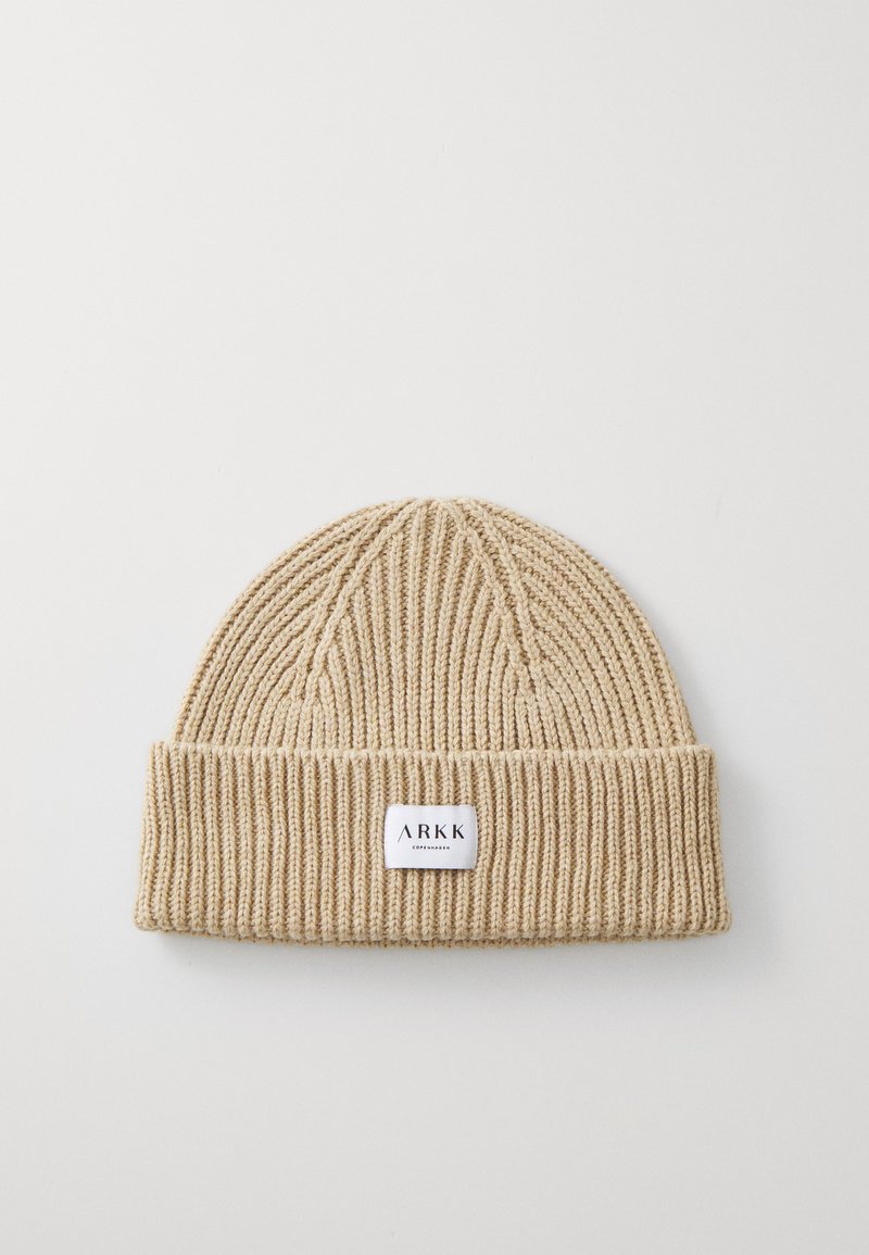 Bonnet beige en tricot avec une texture côtelée et un revers replié. Présente une petite étiquette blanche avec "ARKK" et "Copenhague."