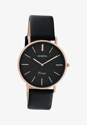Montre ronde noire avec boîtier en or rose, index horaires minimaux, bracelet en cuir noir, et texte "OOZOO Vintage" sur le cadran.