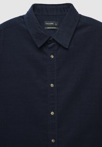 Camicia di velluto a coste blu navy con colletto button-down, caratterizzata da sei bottoni metallici sulla parte anteriore e un'etichetta con vestibilità regolare all'interno del colletto.
