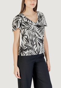 Blusa a maniche corte in bianco e nero con scollo a V e stampa fogliame. Indossata con pantaloni neri, evidenziando una vestibilità ampia e una texture morbida.