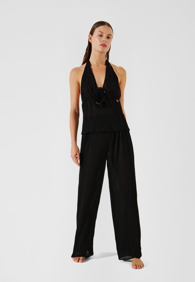 Haut noir à col licou avec un design en couches et un détail floral central, associé à un pantalon noir à jambes larges, fabriqué dans un tissu léger.