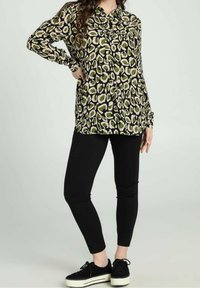 Maglietta nera a maniche lunghe con motivo astratto verde e beige, abbinata a leggings neri e sneakers platform nere. Design semplice.