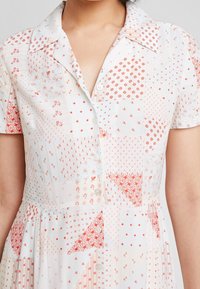 Short-sleeve dress in lightweight fabric with a white base and red patterns, featuring a buttoned front and a fitted bodice.