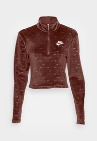 Brun velour zip-up tröja med hög krage, med ett upprepat "NIKE AIR" logotypmönster och en vit Nike-logotyp på bröstet.
