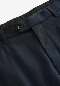 Pantalon bleu marine à la texture lisse, avec des plis sur le devant et une fermeture à bouton unique à la taille. Comprend une fermeture éclair dissimulée.
