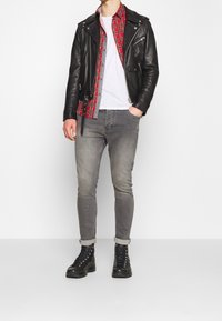 Black leather biker jacket layered over a red plaid shirt, worn with a white t-shirt, grey skinny jeans, and black lace-up boots.