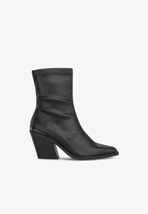 Botas de tobillo negras de cuero suave con punta afilada, silueta elegante y un bloque de tacón distintivo. Costura decorativa en la parte superior.