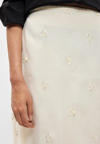 Saia de cor creme com bordados florais intrincados e detalhes em contas, feita de um tecido leve e texturizado.