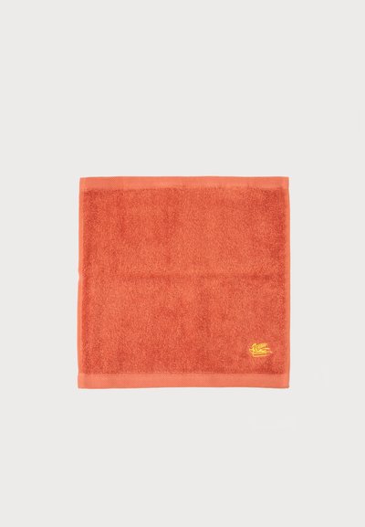 Serviette carrée en éponge orange avec un petit logo jaune brodé dans le coin inférieur droit sur fond blanc.