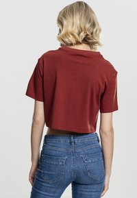 Cropped rust red t-shirt with short sleeves, made of soft fabric. Paired with blue high-waisted jeans, showcasing a fitted design.