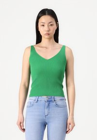 Groene geribbelde tanktop met een V-hals en brede bandjes, gecombineerd met lichtblauwe skinny jeans. Glad textuur, aangesloten ontwerp.