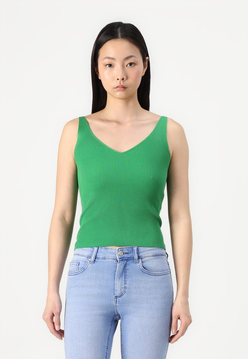 Groene geribbelde tanktop met een V-hals en brede bandjes, gecombineerd met lichtblauwe skinny jeans. Glad textuur, aangesloten ontwerp.