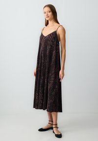 Ein dunkelbraunes, gemustertes Maxikleid mit dünnen Trägern und einer ausgestellten Silhouette. Der Stoff hat eine strukturierte Optik und weist ein zebraähnliches Design auf.