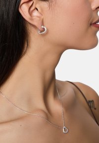 Orecchini a forma di cuore in argento con accenti di gemme, abbinati a una delicata collana in argento con un ciondolo a forma di cuore coordinato.