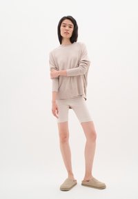 Svijetlo bež oversized džemper, kremasti uski šortsevi i bež slip-on cipele. Mekane teksture, opušteni kroj, minimalistički dizajn i neutralne boje.