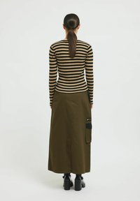 Top ajustado a rayas negras y beige con mangas largas, combinado con una falda maxi verde oliva que tiene un bolsillo lateral y un detalle de cremallera negra.