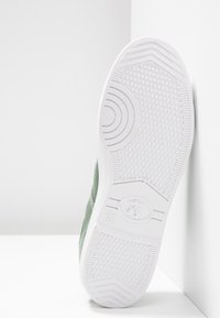 Sneaker in tessuto verde con suola in gomma bianca. L'esterno presenta un motivo testurizzato per una migliore aderenza e linee curve per un tocco di design aggiuntivo.