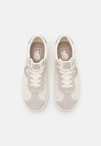 Baskets Vans en daim beige clair, avec des accents gris, des lacets blancs et une semelle en caoutchouc, ornées d'un logo sur la languette et la semelle intérieure.