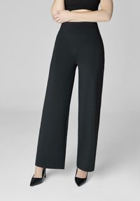 Czarne spodnie o szerokich nogawkach wykonane z gładkiego materiału, z wysokim stanem i prostym, schludnym krojem, zestawione z czarnymi szpiczastymi szpilkami.
