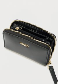 Sort læderpung med guldlås og "HUGO"-logo, delvist åben med en indvendig lynlåslomme og kortlommer.