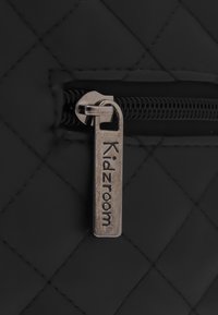 Černá prošívaná látka s kovovým zipem, na kterém je vyryto "Kidzroom". Zip má texturovaný design, který zajišťuje lepší úchop.