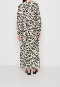 Robe longue à motifs floraux crème avec des accents noirs et verts ; dotée de longues manches, d'un col rond et d'une silhouette décontractée.