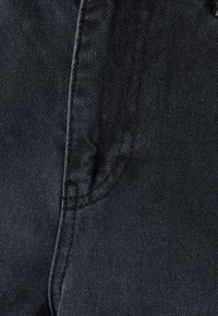 Svart denimtyg med en subtil textur, med kontrasterande sömmar och en sömdetalj som antyder en figurnära design.