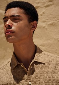 Chemise beige clair texturée avec un motif diagonal et un col classique. Dotée de boutons blancs sur la patte de boutonnage avant.