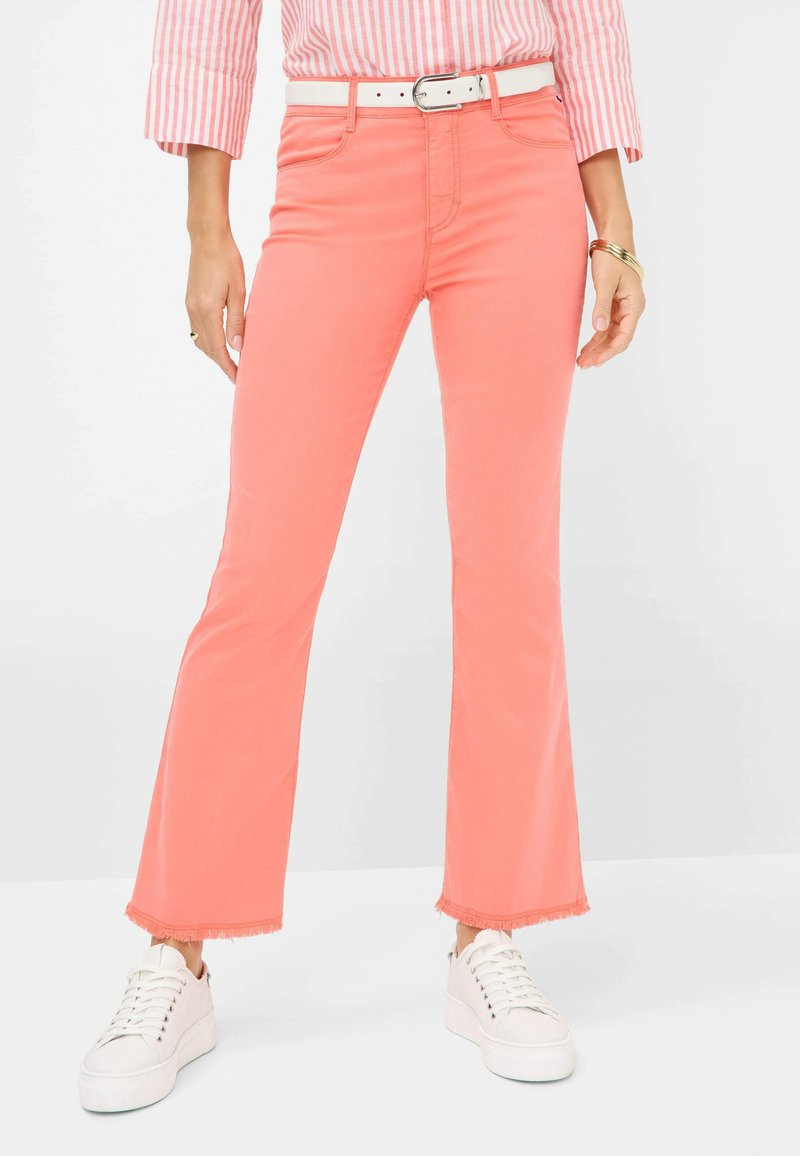 Les jeans évasés corail présentent une taille haute, des ourlets effilochés et sont associés à une ceinture blanche et des baskets pour un look décontracté.