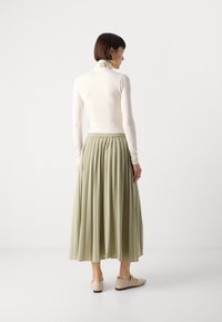 Lettvekts kremfarget langermet topp med brodert krage, parret med en plisserte, ankel-lange, lys grønn skjørt og beige slip-on sko.