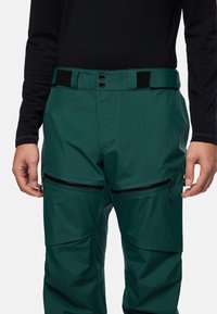 Groene skibroeken hebben een gestructureerd oppervlak, een verstelbare taille met zwarte klittenband, ritszakken en een ontspannen pasvorm.