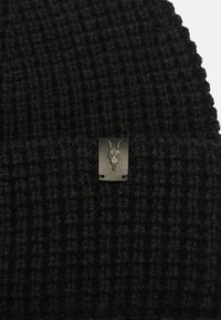 Berretto lavorato a maglia nero con un motivo a coste testurizzate, dotato di un'etichetta in pelle nera con un design di teschio di capra in rilievo.