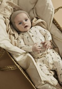 Helles beiges Babyoutfit mit Drachenmuster, bestehend aus einem knöpfbaren Oberteil und passenden Hosen. Eine gestrickte Mütze und eine strukturierte Decke sind ebenfalls enthalten.