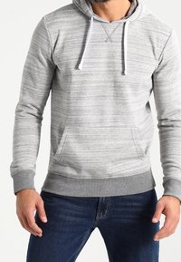 Sudadera con capucha gris a rayas con un bolsillo canguro delantero, cordones blancos, puños y dobladillo inferior acanalados, usada sobre unos vaqueros azules.