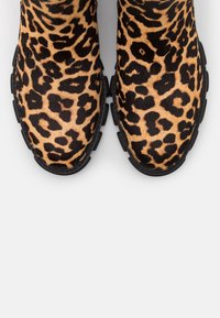 Une paire de chaussures à imprimé léopard avec des orteils ronds et des semelles en caoutchouc noir sur une surface blanche.